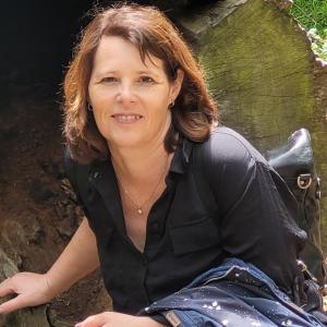 Frau in schwarzer Bluse kniet neben einem großen Baumstumpf